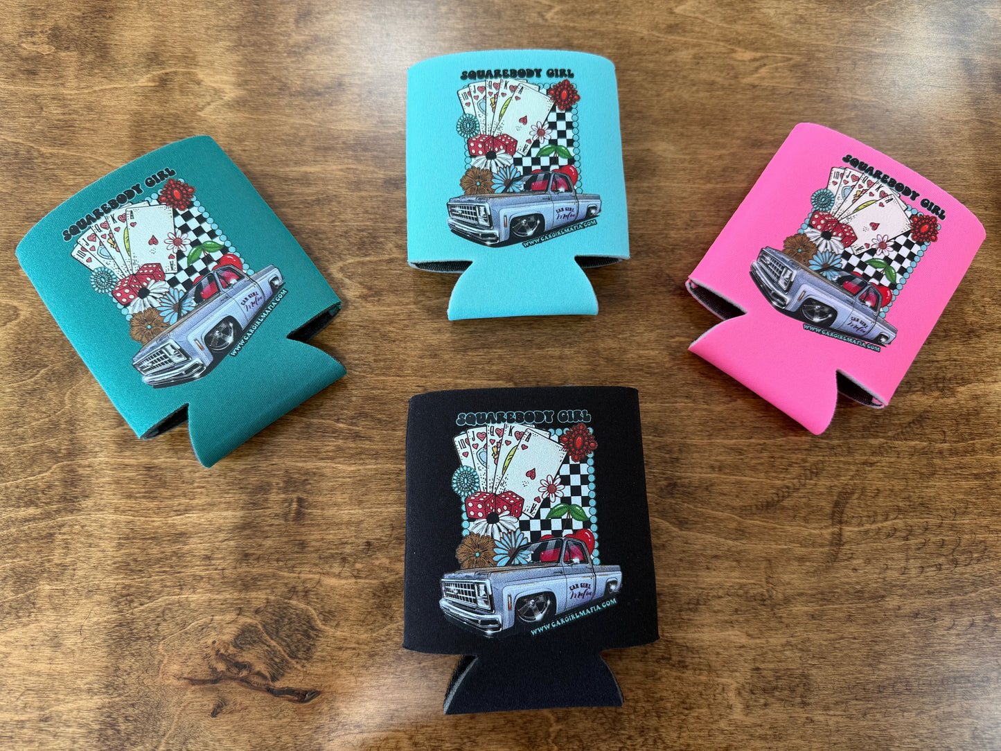 Four can coolers with graphic designs on a wooden surface