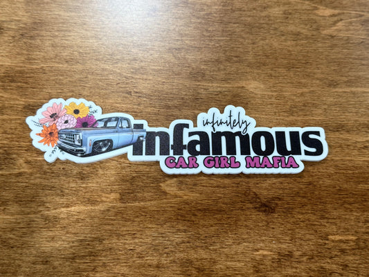 Sticker with 'infinitely infamous car girl mafia' text on a wooden surface